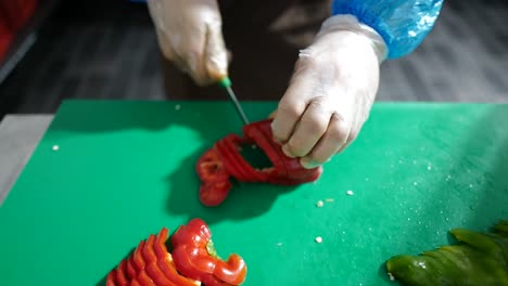 Close-up-of-chef's-hand-chopping-red-paprika-on-a-wooden-cutting-board