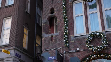 Tilt-up-shot-of-people-walking-by-facade-of-old,-Dutch-buildings-in-Amsterdam,-Netherlands