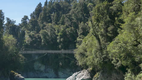 Slow-Motion-pan-down-over-a-bridge-across-a-turquoise-blue-river---Hokitika-Gorge,-New-Zealand