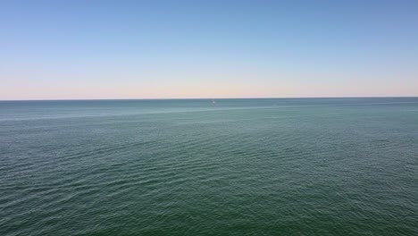 Aerial-view-over-calm-ocean-with-single-small-sailboat-in-vast-seascape