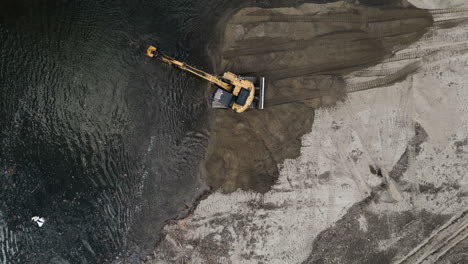 Drone-rises-to-reveal-an-excavator-removing-sediment-from-a-river-flowing-on-Sandy-bank