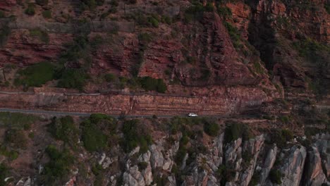 Coche-Que-Viaja-En-Chapman&#39;s-Peak-Drive-Después-Del-Atardecer-En-Ciudad-Del-Cabo,-Sudáfrica---Disparo-Aéreo-Con-Drones