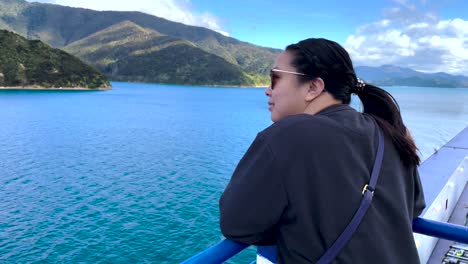 Blick-über-Die-Schulter-Einer-Asiatischen-Frau,-Die-Von-Einem-Boot-In-Neuseeland-Aus-Auf-Bewaldete-Inseln-Und-Wasser-Blickt