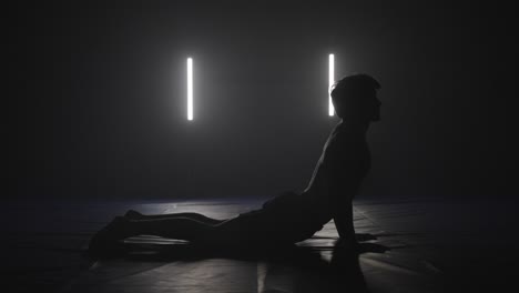 Sphinx-Yoga-Pose,-Ausgeführt-Von-Einem-Männlichen-Kämpfer-Im-Dunklen-Studio,-Silhouette-Yoga-Pose