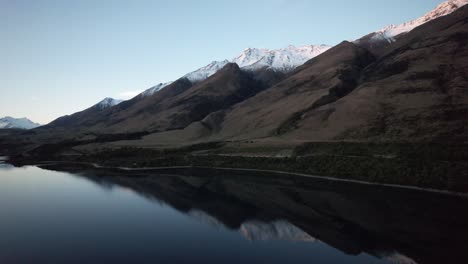 Vuelo-Aéreo-Hacia-Montañas-Cubiertas-De-Nieve-Perfectamente-Reflejadas-Al-Atardecer-Cerca-De-Queenstown,-Nueva-Zelanda