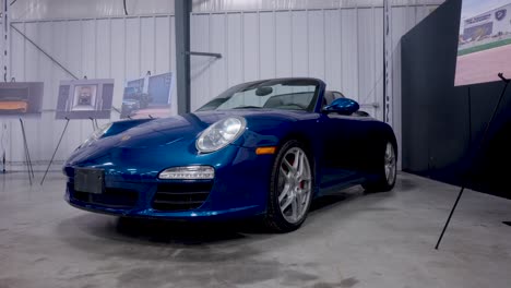 Disparo-Estático-De-Un-Coche-Deportivo-Porsche-Convertible-Azul-Metálico-Dentro-De-Una-Exposición-De-Vehículos-Automotores-En-Interiores