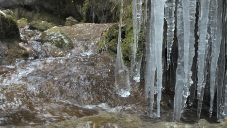 Corriente-De-Agua-Clara-Que-Fluye-Desde-Los-Alpes-Con-Carámbanos-Colgantes-En-La-Naturaleza,-Primer-Plano