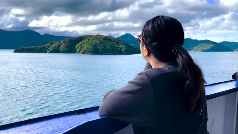 Dark-haired-woman-lost-in-thought-stares-from-boat-out-at-islands-and-blue-bay-waters-in-New-Zealand