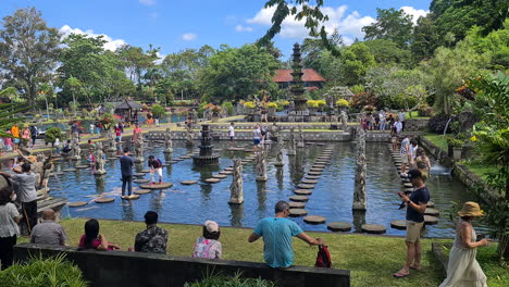 Tirta-Gangga-Water-Palace,-Bali-Island,-Indonesia,-People-on-Stepping-Stones-in-Pond-Full-of-Carp-Fish