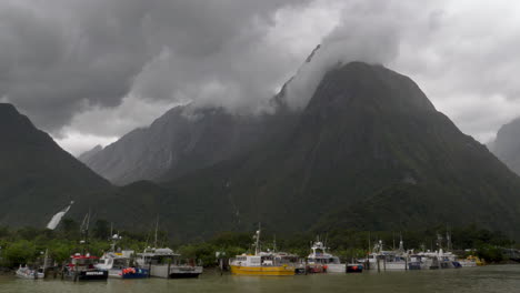 4K-footage-of-a-fleet-of-fishing-boats-beneath-a-cloudy-mountain-in-Milford-Sound---Piopiotahi,-New-Zealand