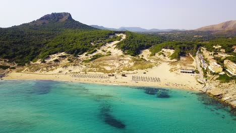 Drone-panning-from-the-left-to-the-right-of-the-coastline-of-Cala-Mesquida,-showing-the-whole-stretch-of-the-coastline-and-mountainous-woodlands-in-the-distance,-in-the-island-of-Mallorca,-Spain