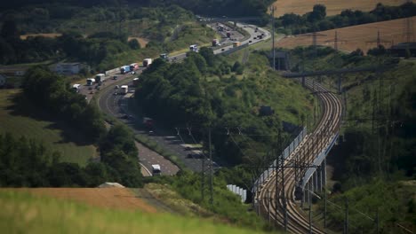 üppiges-Grün-Flankiert-Eisenbahn-Und-Autobahn-Im-Sonnenlicht,-Transport-Im-Einklang-Mit-Der-Natur,-Entfernte-Perspektive