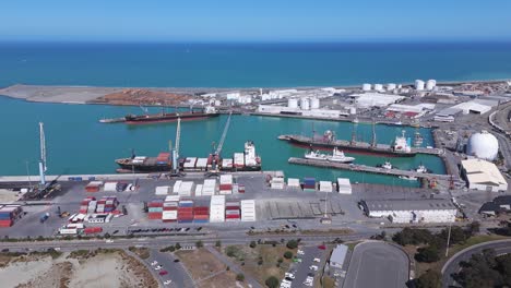 Timaru-port-in-new-zealand,-containers-and-ships-docked,-blue-ocean,-sunny-day,-industrial,-aerial-view