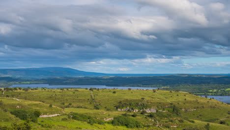 Timelapse-of-rural-nature-farmland-with-stonewall-on-hillside-and-lake-in-distance-during-sunny-day-with-clouds-in-the-sky-viewed-from-Carrowkeel-in-county-Sligo-in-Ireland