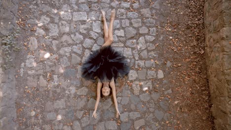 Pretty,-sensual-ballet-dancer-lying-on-a-cobbled-ground-stretching-her-body