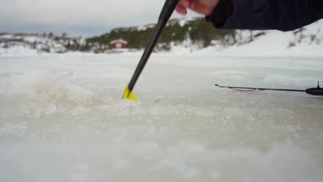 El-Hombre-Está-Utilizando-Un-Skimmer-De-Hielo-Durante-Su-Expedición-De-Pesca-En-Hielo-En-Bessaker,-Condado-De-Trondelag,-Noruega---Primer-Plano