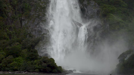 Slow-Motion-static-footage-of-the-bottom-of-a-waterfall-in-Milford-Sound-with-trees---Piopiotahi,-New-Zealand