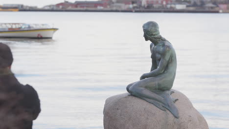 Tourists-visiting-The-Little-Mermaid-statue-and-ferry-boat-passing-behind