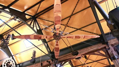 A-giant-mechanically-operated-wooden-ceiling-fan-rotates-in-a-huge-warehouse-with-heavy-steam-punk-influence-in-the-design