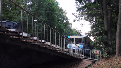 White-and-blue-funicular-going-down-a-steep-slope-railroad-in-a-green-park-in-Kyiv-city-Ukraine,-public-transport,-4K-static-shot