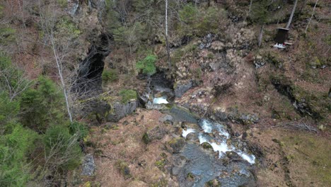 Fließendes-Wasser-Stürzt-Zwischen-Großen-Felsbrocken-In-Einer-Wiesenlichtung-Mit-Kahlen-Bäumen-Herab