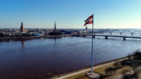 A-flagpole-stands-in-front-of-a-city-and-body-of-water,-Daugava-river