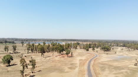 Aerial-shot-of-barren-land-with-asphalt-road-and-water-at-a-distance-in-Charu-village-in-Chatra,-Jharkhand,-India