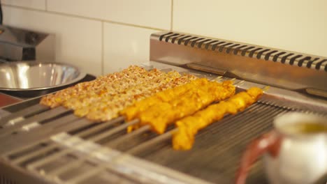 Brochetas-De-Pollo-A-La-Parrilla-Chisporroteando-En-Una-Parrilla-De-Kebab,-Iluminación-Cálida