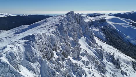 Snow-capped-Bucegi-Mountains-under-clear-blue-sky,-panoramic-aerial-view-in-daylight