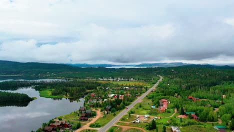 Panoramic-View-of-a-Beautiful-Mountain-Town-in-a-Forest-with-Breathtaking-Cloudy-Hills-in-the-Background-of-a-Peaceful-Clear-Lake-and-Reflection-of-Clouds-on-the-Water