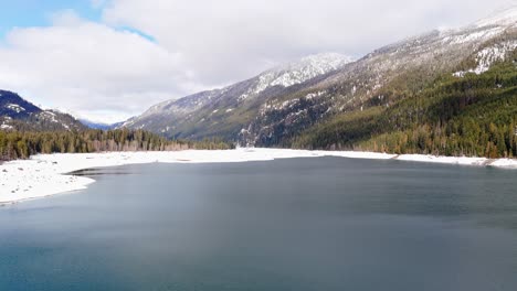 Backwards-drone-footage-in-4K-of-snow-capped-mountains-in-Lake-Kachess,-Washington-State