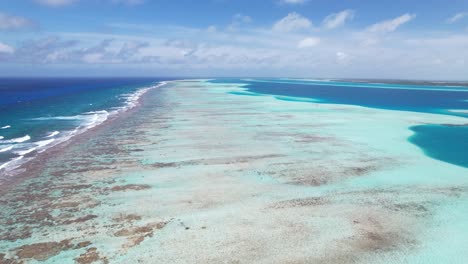Vibrant-coral-reef-beside-azure-waters-under-a-clear-sky,-forward-moving-shot,-aerial-view