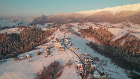 Sunrise-glows-over-Pestera-Village-with-snow-covered-roofs,-aerial-winter-wonderland