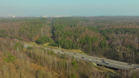 highway-cuts-through-the-forest-on-its-approach-to-Gdynia,-aerial-shot,-with-the-treeline-receding-towards-the-city,-reflecting-a-blend-of-natural-and-urban-environments