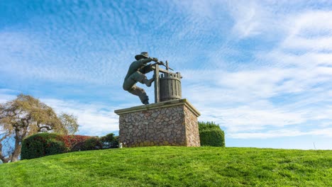 The-Napa-Valley,-The-Grape-Crusher-sculpture-Timelapse-with-clouds-moving-back-and-in-a-vibrant-environment-with-a-blue-sky-and-green-grass