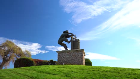 The-Napa-Valley,-The-Grape-Crusher-sculpture-pull-back-on-cloudy-day-with-vibrant-sky