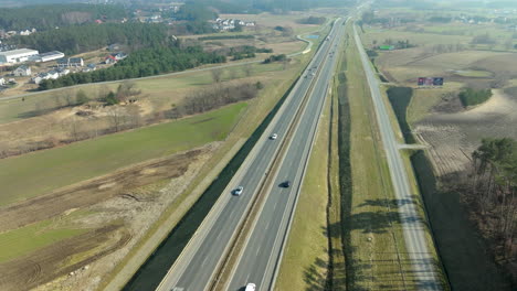 Aerial-view-of-vehicles-on-a-highway-cutting-through-a-rural-landscape