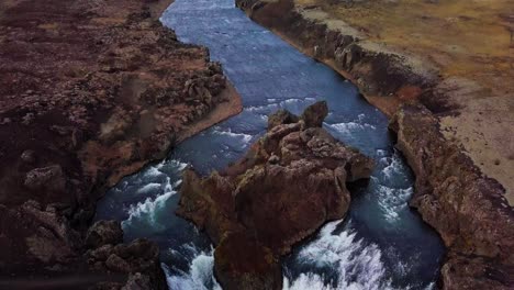 Tilt-down-aerial-shot-of-blue-river-separating-into-twin-waterfalls-in-Iceland