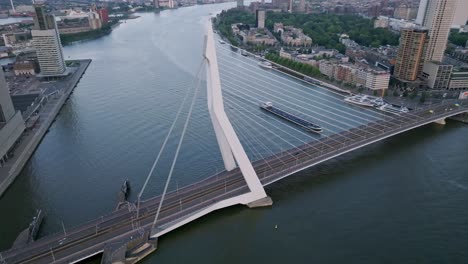 Tilting-down-drone-shot-boat-passing-underneath-Erasmus-bridge,-Rotterdam
