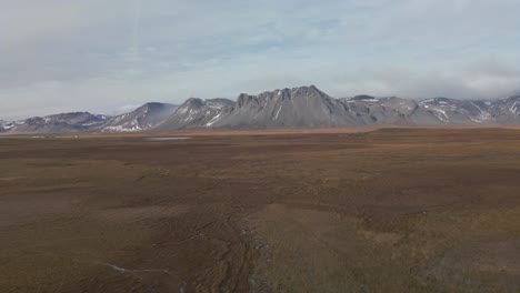 Flying-towards-dramatic-mountain-range-towering-in-deserted,-icelandic-countryside