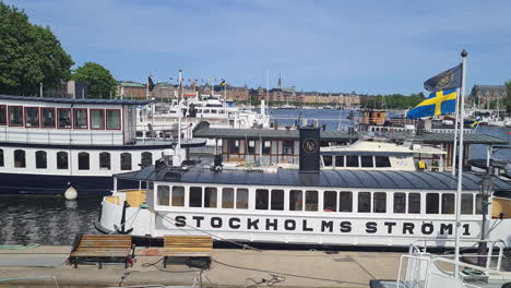 Moored-Boats-With-Swedish-National-Flag-in-Djurgarden-Neighborhood-of-Stockholm,-Sweden-on-Sunny-Summer-Day