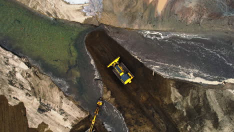 Ascending-top-down-aerial-view-of-bulldozer-and-excavator-moving-soil-in-front-of-water-channel-at-pond-site