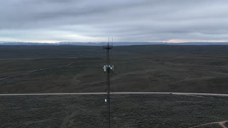 Die-Drohne-Fliegt-Rückwärts-über-Die-Kahle-Wüstenlandschaft-Von-Einem-Sehr-Hohen-Handymast-An-Einem-Späten,-Bewölkten-Winterabend.