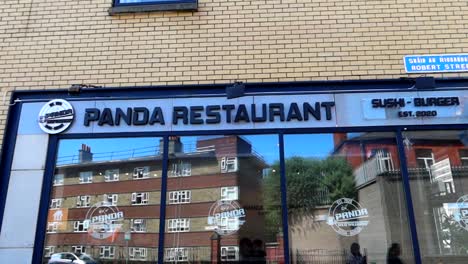 Panning-shot-of-Panda-restaurant-facade-with-big-windows-reflecting-buildings-and-blue-sky