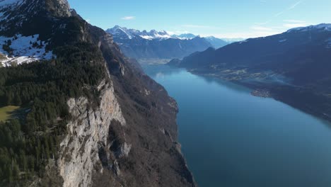 Drohne-Kippt-Nach-Unten-Entlang-Steiler-Bergklippen-Und-Atemberaubendem-Blauen-Wasser,-Das-Den-Sonnigen-Himmel-Im-Walensee,-Walensee,-Schweiz,-Reflektiert