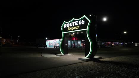 Zeitraffervideo-Des-Großen-Route-66-Schildes-In-Kingman,-Arizona-Bei-Nacht-Mit-Vorbeifahrenden-Menschen-Und-Fahrzeugen