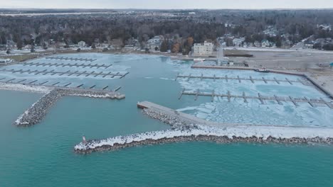 Icy-port-elgin-harbor-with-frozen-piers,-blue-water,-and-coastal-town-backdrop,-at-dusk,-aerial-view
