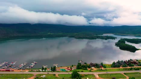 Luftaufnahme-Eines-Reservoirs-Aus-Der-Vogelperspektive-Auf-Den-Shadow-Mountain-Reservoir-Und-Den-Grand-Lake-Mit-Wunderschöner-Spiegelung-Der-Berge-Und-Sanften-Wolken,-Während-Autos-Auf-Dem-Colorado-Highway-Entlang-Der-Bewölkten-Küste-Fahren