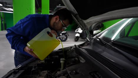 Mechanic-with-beard-and-glasses-fill-up-windshield-wiper-fluid-in-garage