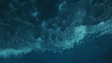 Brechende-Welle-Stürzt-Ab,-Während-Sich-Blasen-über-Die-Meeresoberfläche-Ausbreiten-Und-In-Einem-Wirbel-Wirbeln,-Unterwasserwinkel